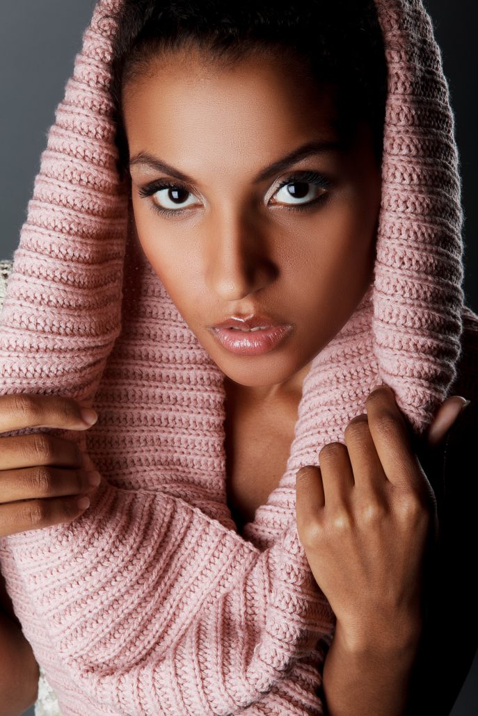 Portrait of beautiful dark-skinned girl with a knitted scarf on a grey background